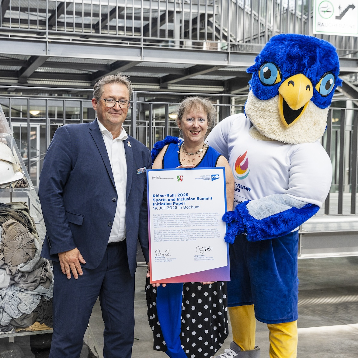 Andrea Milz mit dem Maskottchen der RR2025 und Jörg Forster links