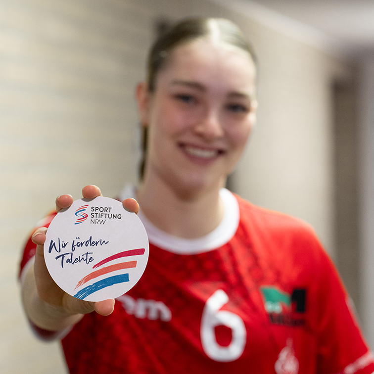 Athletin in rotem Shirt hält Sportstiftung NRW-Plakette