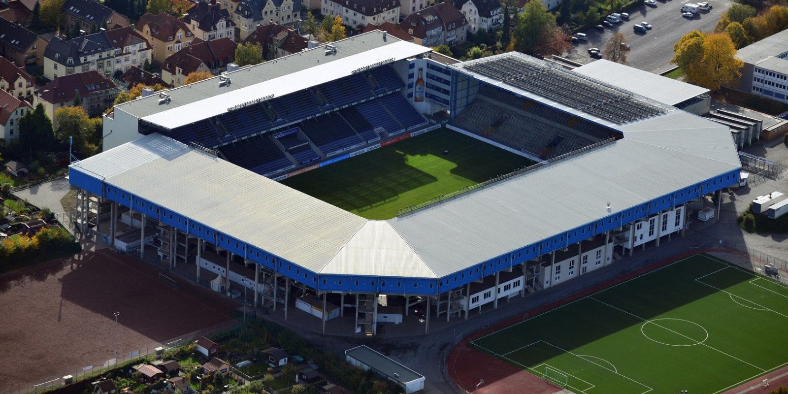 Stadion SchücoArena Bielefeld aus der Vogelperspektive. Ein offenes Stadion mit überdachtern Tribühenen, die Außenfassade ist blau.