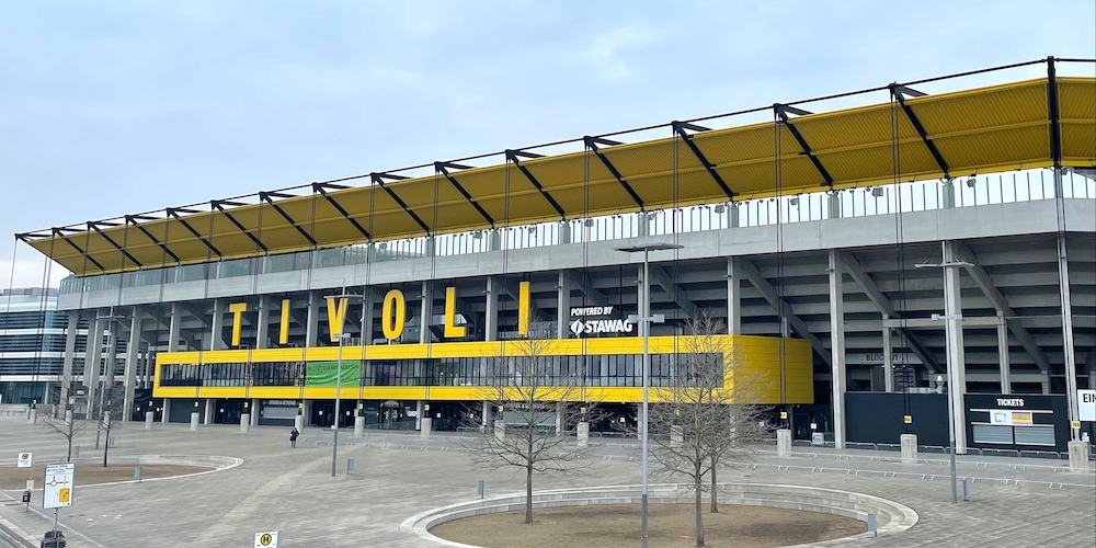 Tivoli  Stadion Aachen aus der Außenansicht. Der Name sowie Elemente der Außenfassade sind sonnengelb gefärbt.
