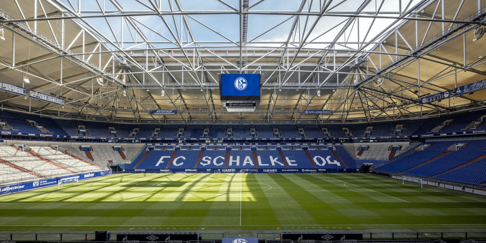 Stadion VELTINS-ARENA in Gelsenkirchen aus der Innenansicht. Königsblaue Stadionsitze, sowie der grüne Rasenplatz sind zu sehen.