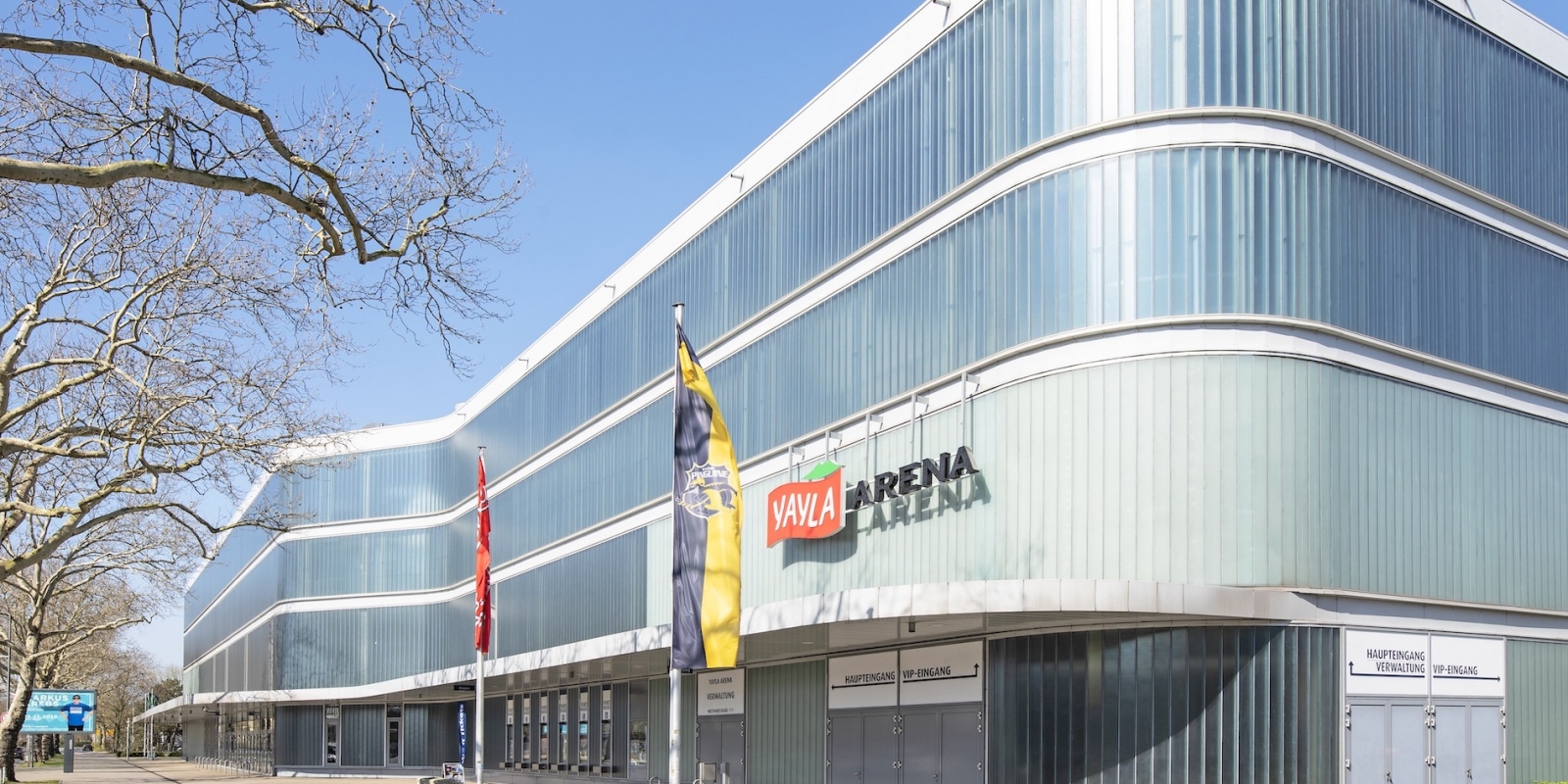 Sporthalle YAYLA-ARENA Krefeld aus der Außenansicht. Es ist weiß mit sehr vielen schmalen, intransparenten Glaselementen.