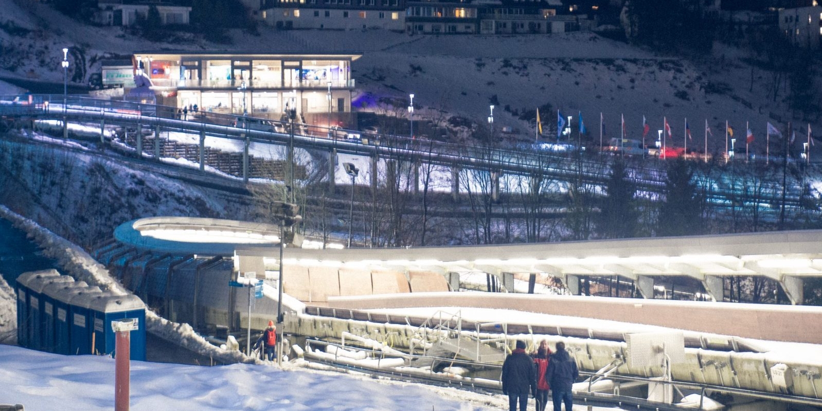 Eine Eisbobbahn an einem Schneebedecktem Hang. Die Bahn ist mit Flutlichtern beleuchtet.