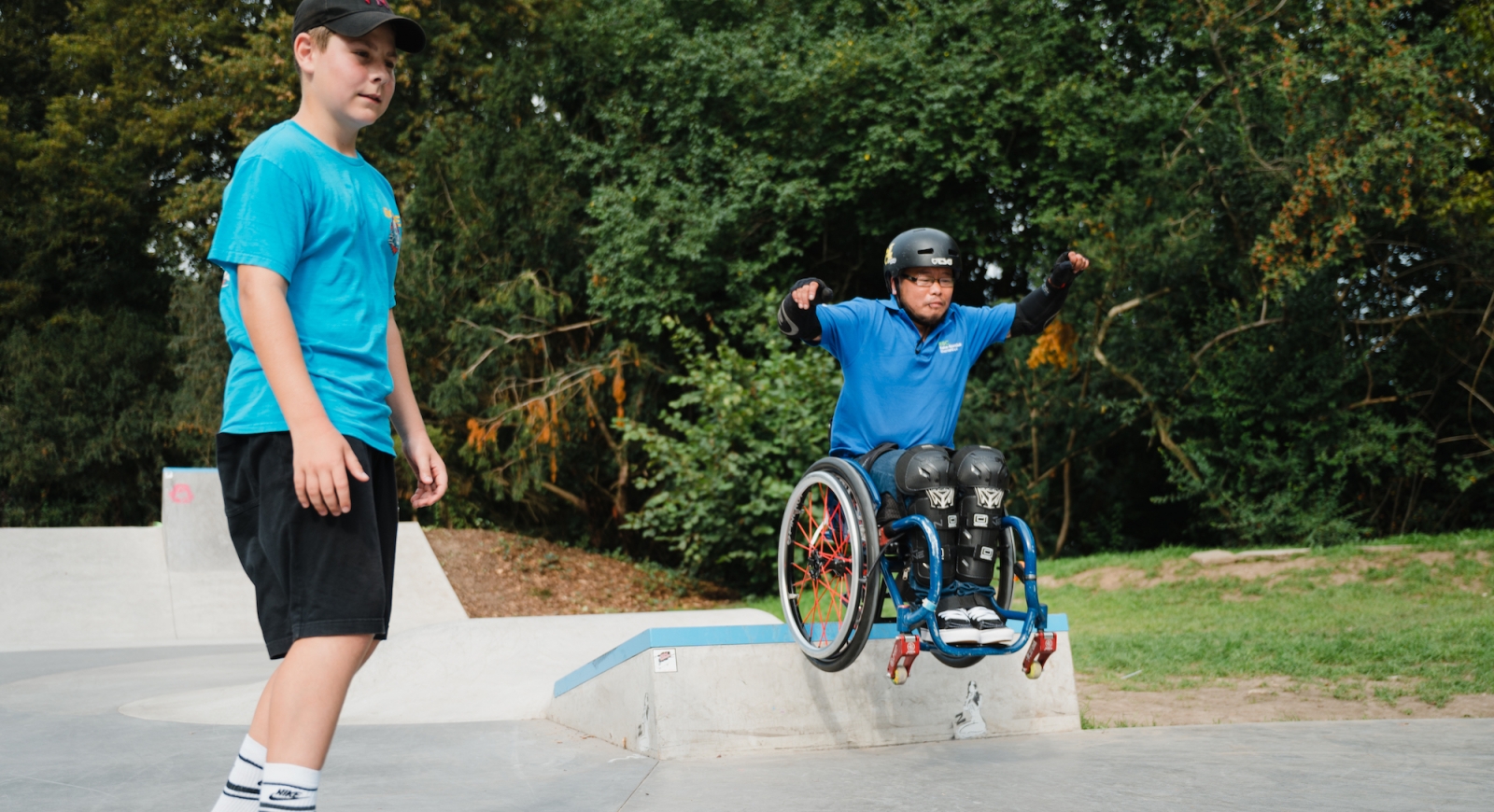 Zwei Skater auf dem Skatepark. Einer auf dem Skateboard einer im Rollstuhl