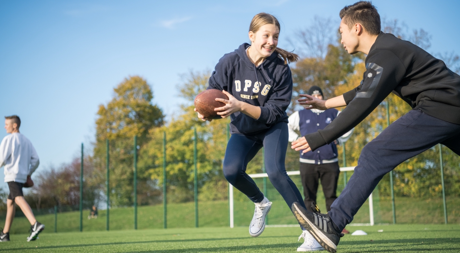 Ein junges Mädchen hält einen Football und versucht an einem jungen Mann vorbeizulaufen.