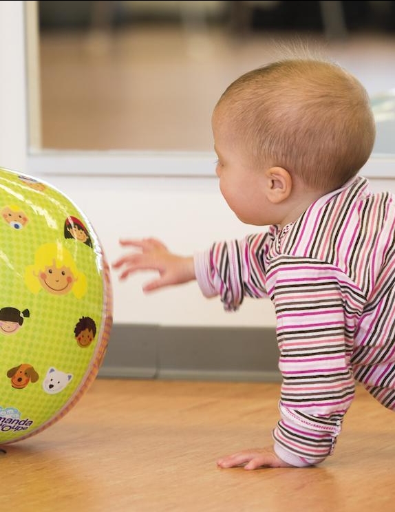 Ein Baby krabbelt einem gelben Ball hinterher