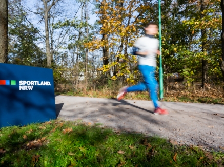 Ein Jogger läuft an einem Sportland.NRW-Schild vorbei