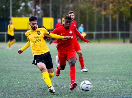 Zwei Fußballer, einer im gelben, der andere im roten Trikot, im Zweikampf um den Ball während eines Spiels.