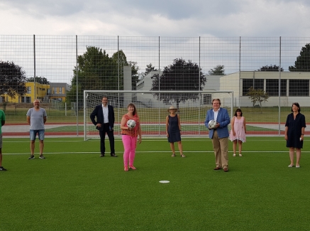 Staatssekretärin Andrea Milz mit Vereinsmitgliedern auf einen Fußball-Rasenplatz. Hinter ihnen steht ein weißes Fußballtor.