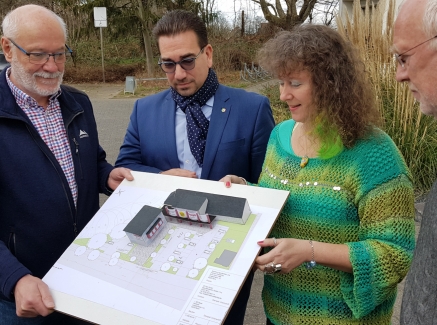 Staatssekretärin Milz (rechts) schaut sich mit drei Herren vom Badminton Club  einen Bauplan an. Sie stehen gemeinsam im Freien.