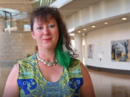 Staatssekretärin Milz in einem blau-grünem Kleid steht in einem großen Foyer, rechts an der Wand hängen einige Kunstgemälde.