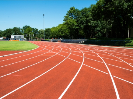 Außen-Sportstadion mit einer 8-bahnigen, roten Tartanbahn, umgeben von Bäumen.