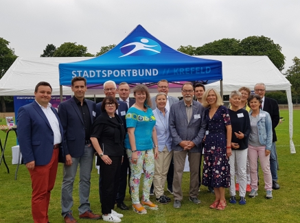 Staatssekretärin Milz steht mit Mitgliedern des Stadtsprotbundes Krefeld draußen auf einem Rasen-Fußballplatz.