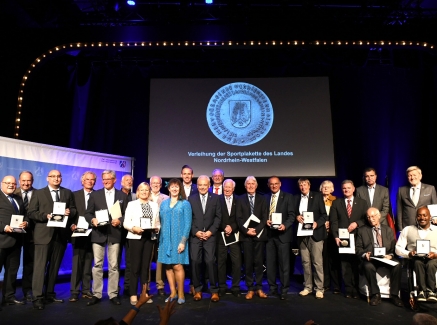 Gruppenfoto auf einer Bühne mit Staatssekretärin Milz im hellblauen Kleid und allen Trägern der Sportplakette.