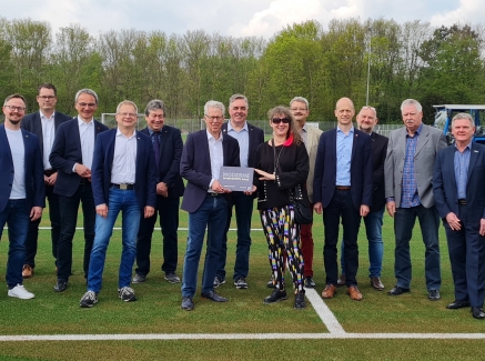 Staatssekretärin Milz steht mit einer Gruppe auf einem Rasen-Fußballplatz