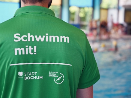 Eine Person im grünen T-Shirts mit der Rückenaufschrift "Schwimm mit!"