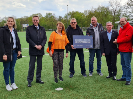 Personen auf Fußballplatz mit Schild Moderne Sportstätte 2022