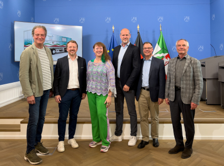 Andrea Milz mit Personen auf einer Bühne bei Vorstellung des Schwimmcontainers "narwali"