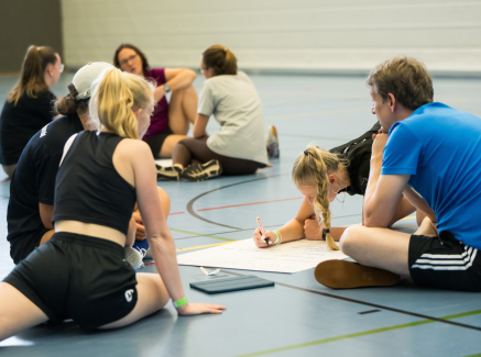 Junge Menschen in einer Sportalle beugen sich über ein Papier