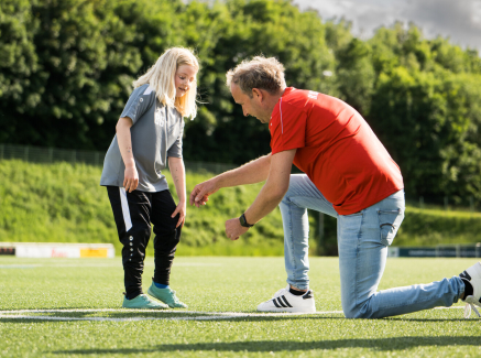 Junger Übungleiter kniet vor einer jungen Sportlerin und erklärt etwas