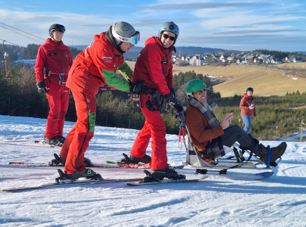Wintersportler mit roten Anzügen schieben eine Person in einem Schlitten