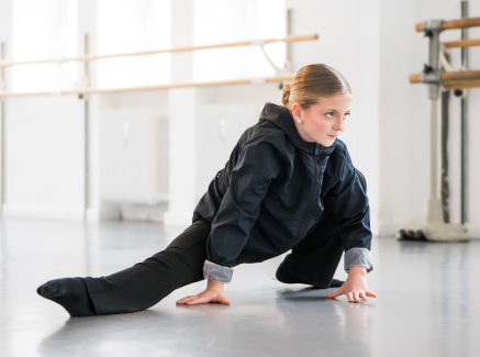 Junge Frau in dunkler Kleidung in Tanzpose mit Händen auf dem Boden in einem Studio