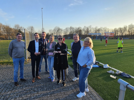 Andrea Milz mit weiteren Personen auf einem Sportplatz bei Sonnenschein und blauem Himmel
