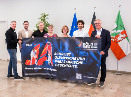 Sieben Personen, darunter Andrea Milz, halten ein Plakat zur Bewerbung KölnRheinRuhr