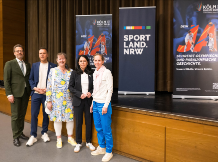 Andrea Milz und weitere vier Personen vor einer Bühne mit Aufstellern zur Bewerbung KölnRheinRuhr