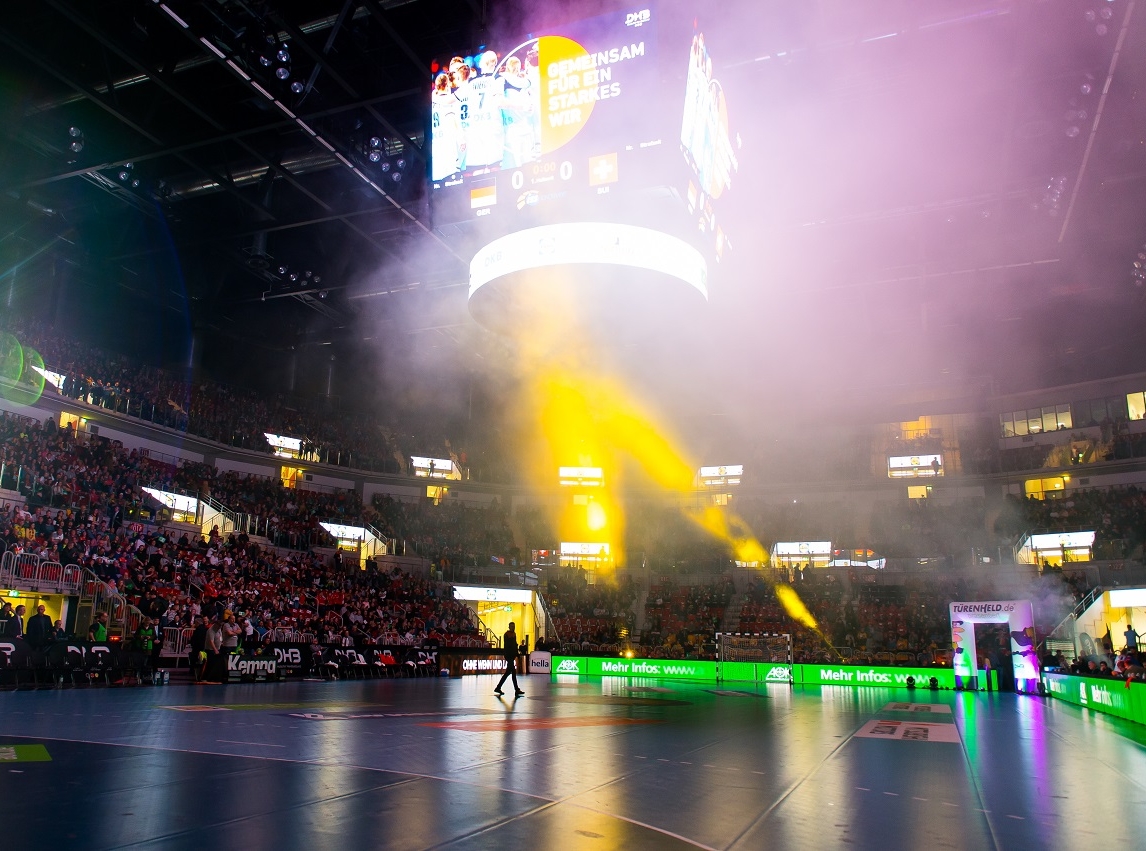 Vollbesetzetes, überdachtes Sportstadion ISS DOME Duesseldorf. Eine Person geht über die Sportfläche. Oben mittig unter der Decke hängt ein vierseitger Bildschimrpräsentator.