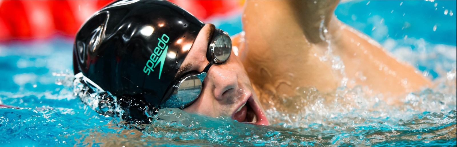 Ein Mann mit einer schwarzen Badekappe und Schwimmbrille krault seine Bahn in einem Schwimmbecken.