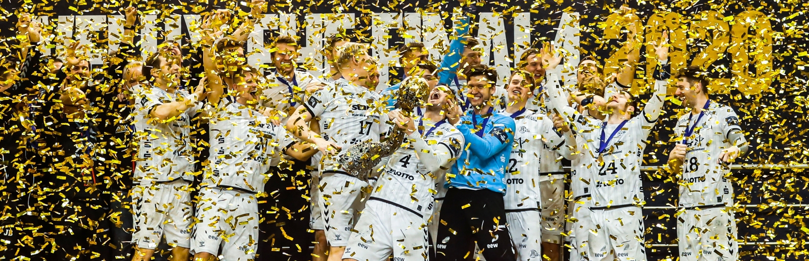 THW Kiel feiern ihren Sieg mit dem EHF Pokal, goldene Lametta regnet von oben herab.