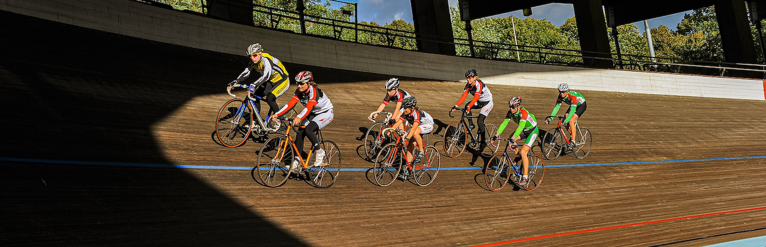 Sieben Rennradsportler fahren mit ihren Rennrädern auf der Radrennbahn des Kölner Radstadions im Sportpark Müngersdorf.