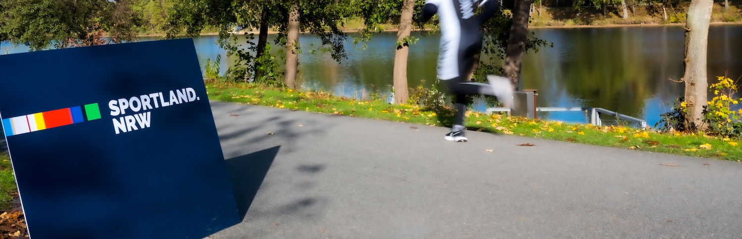 Sportland.NRW-Schild mit vorbeilaufendem Jogger