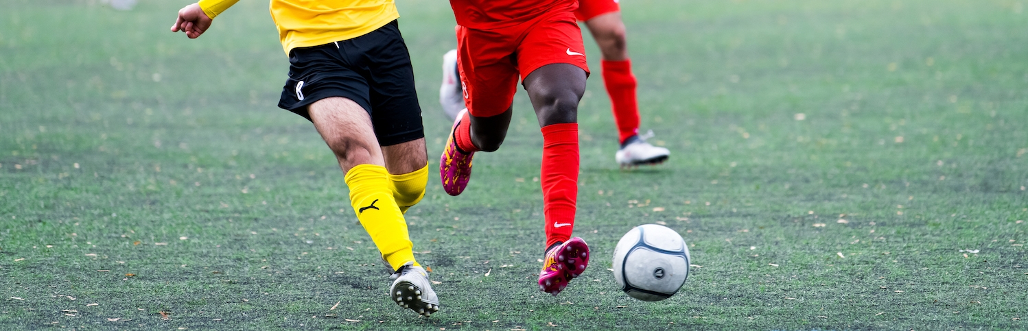 Zwei Fußballer, einer im gelben, der andere im roten Trikot, im Zweikampf um den Ball während eines Spiels.