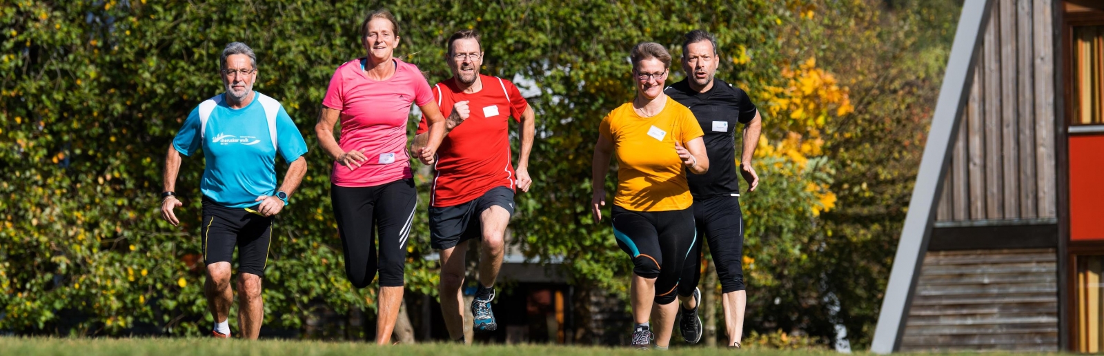 2 ältere Damen und 3 ältere Herren joggen zur Prävention und für Gesundheit über eine Rasenfläche.