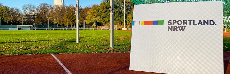 Weißes Sportland.NRW-Schild auf Tartanbahn