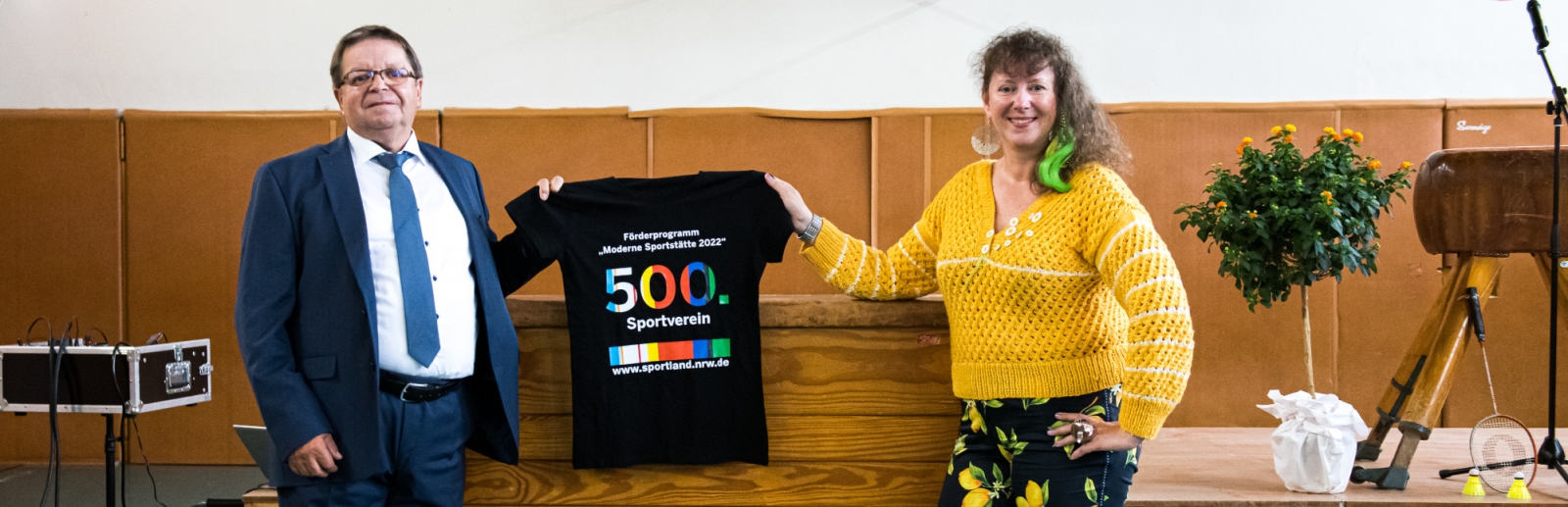 Staatssekretärin Milz hält ein schwarzes T-Shirt mit Logo der Förderung mit der Zahl 500 in Regenbogenfarben.