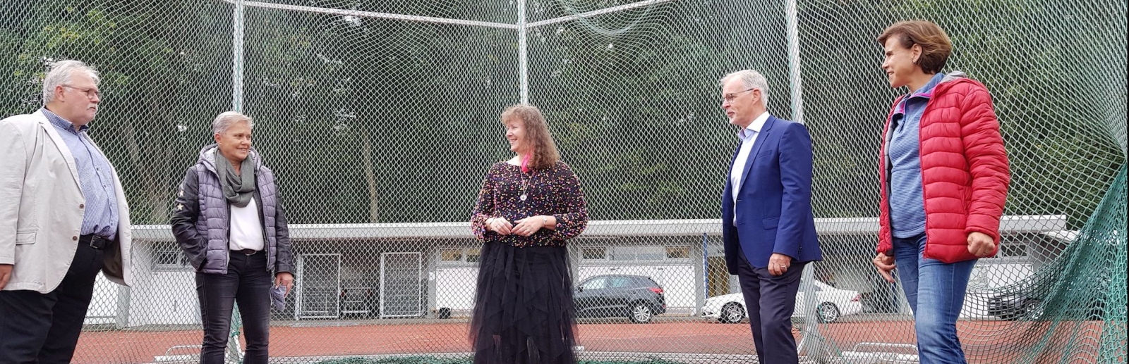 Staatssekretärin Andrea Milz steht mit mehreren Vereinsmitgliedern auf einem Hammerwurf-Sportplatz. Im Hintergrund sieht man das Auffang-Stahlnetz im Halbkreis aufgestellt.