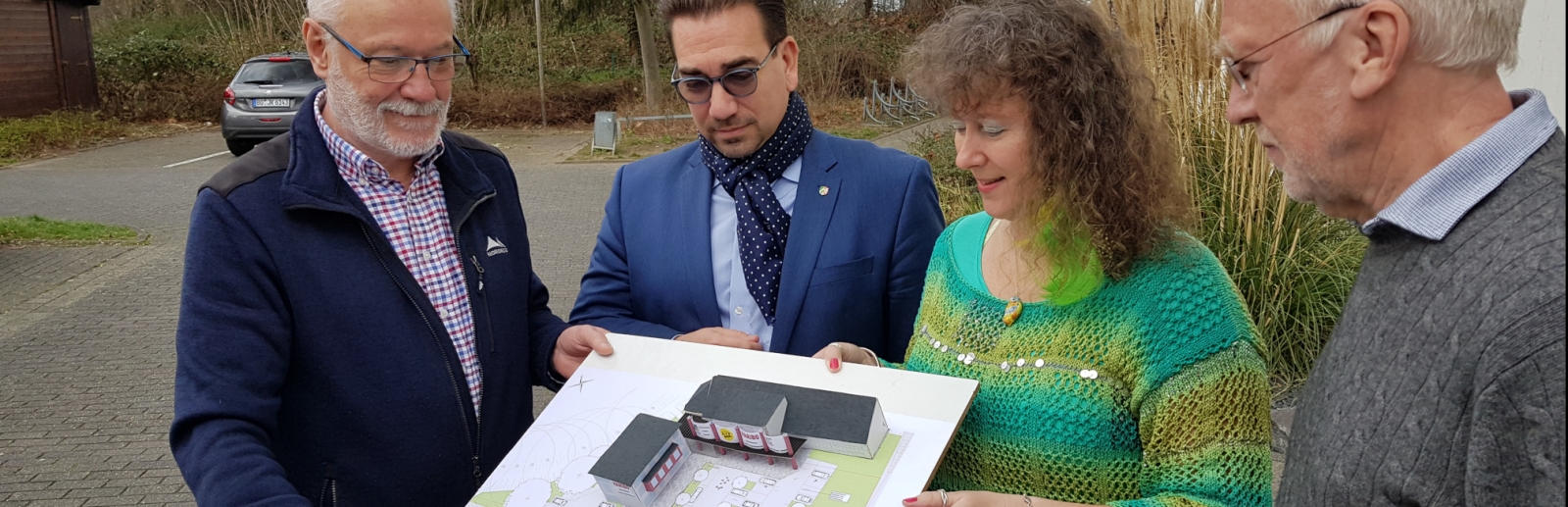 Staatssekretärin Milz (rechts) schaut sich mit drei Herren vom Badminton Club  einen Bauplan an. Sie stehen gemeinsam im Freien.