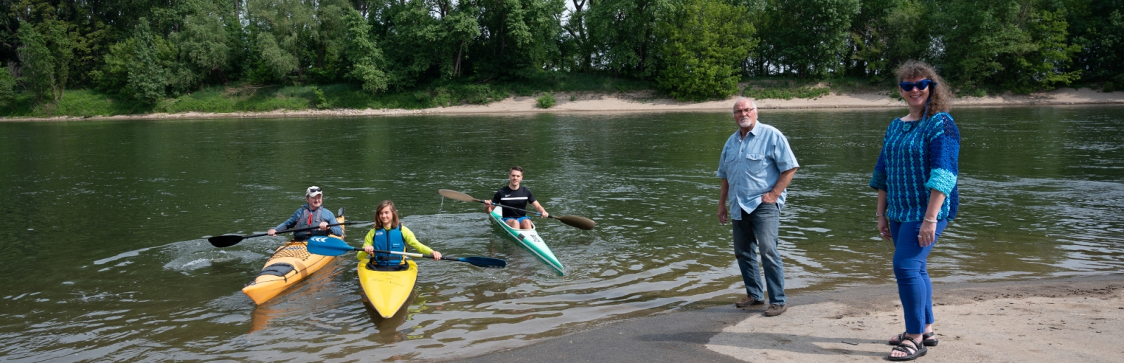 Staatssekretärin Milz steht am Ufer eines Sees. Auf dem See sind drei Kanufahrer. Am gegenüberliegenden Ufer stehen Bäume.