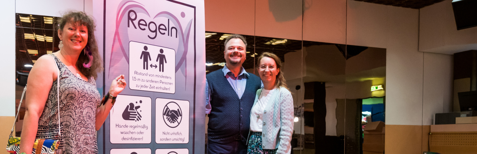 Staatssekretärin Milz steht mit einem Paar an der Hygiene-Plakatwand des Tanzhauses.