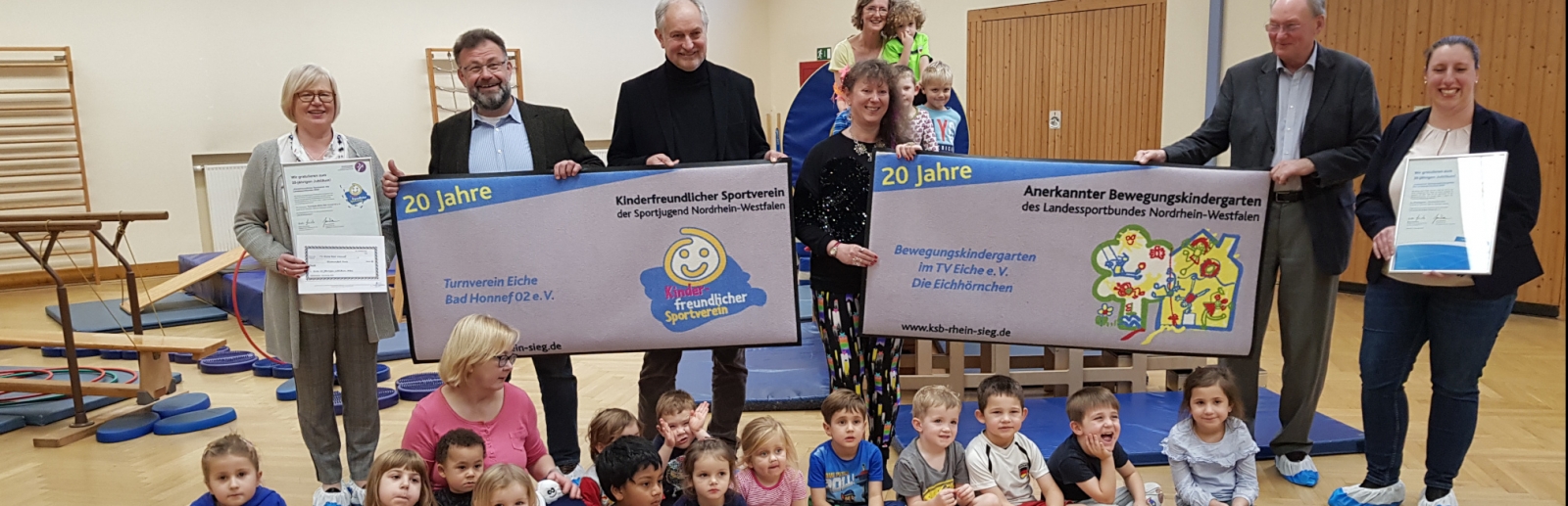 Gruppenfoto mit Staatssekretärin Andrea MIlz, vor ihr sitzen die Kinder der Eichhörnchen-Gruppe auf dem Turnhallenboden.