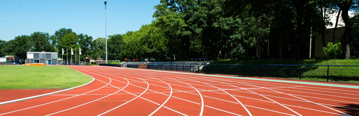 Außen-Sportstadion mit einer 8-bahnigen, roten Tartanbahn, umgeben von Bäumen.