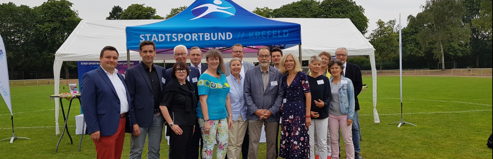 Staatssekretärin Milz steht mit Mitgliedern des Stadtsprotbundes Krefeld draußen auf einem Rasen-Fußballplatz.