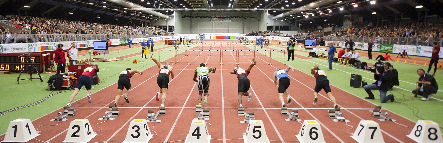 Von hinten betrachtet: Sieben Sprinter starten gerade zum Sprint in einer Indoor-Leichtathletikhalle.