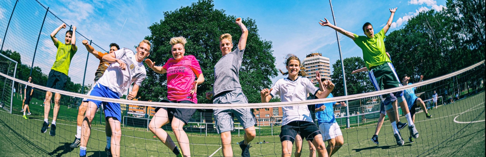 Viele Jungs in Sportkleidung springen vor einem Tennisnetz in die Höhe.