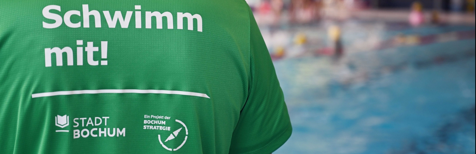 Eine Person im grünen T-Shirts mit der Rückenaufschrift "Schwimm mit!"