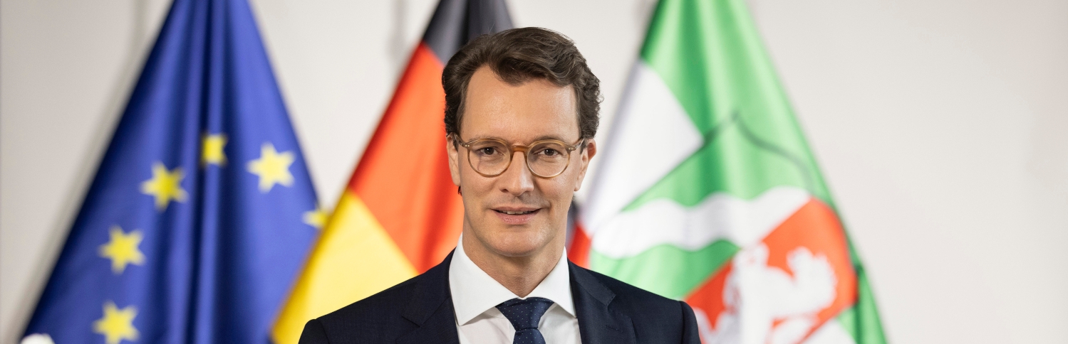 Ministerpräsident Hendrik Wüst vor den Flaggen von Nordrhein-Westfalen, Deutschland und Europa.