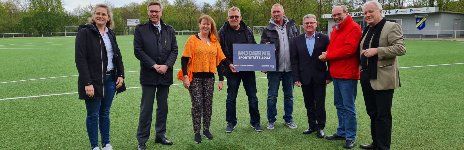 Personen auf Fußballplatz mit Schild Moderne Sportstätte 2022